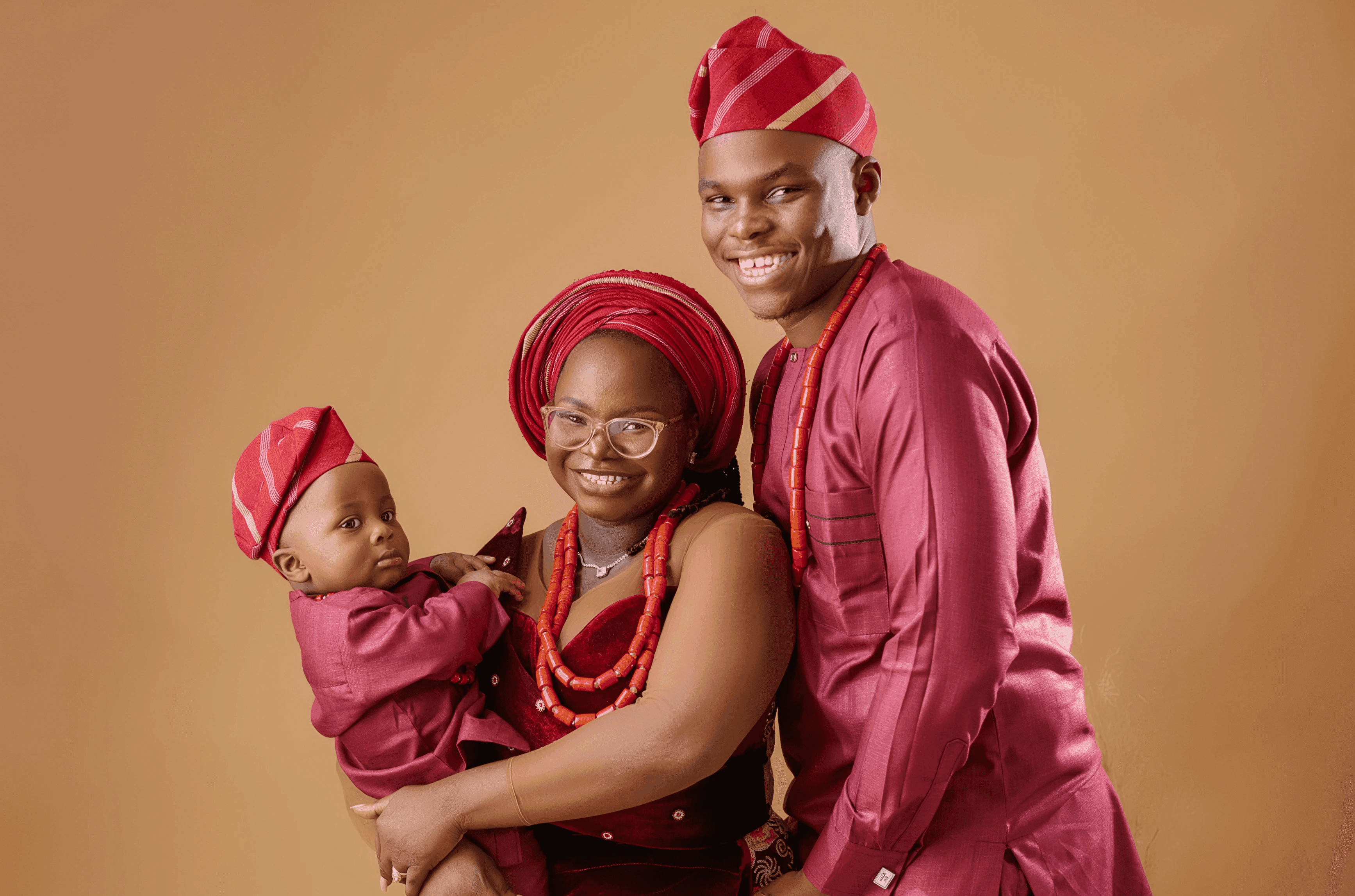 Latte Lawson with his family, all three in matching red traditional dress against a warm ochre backdrop.